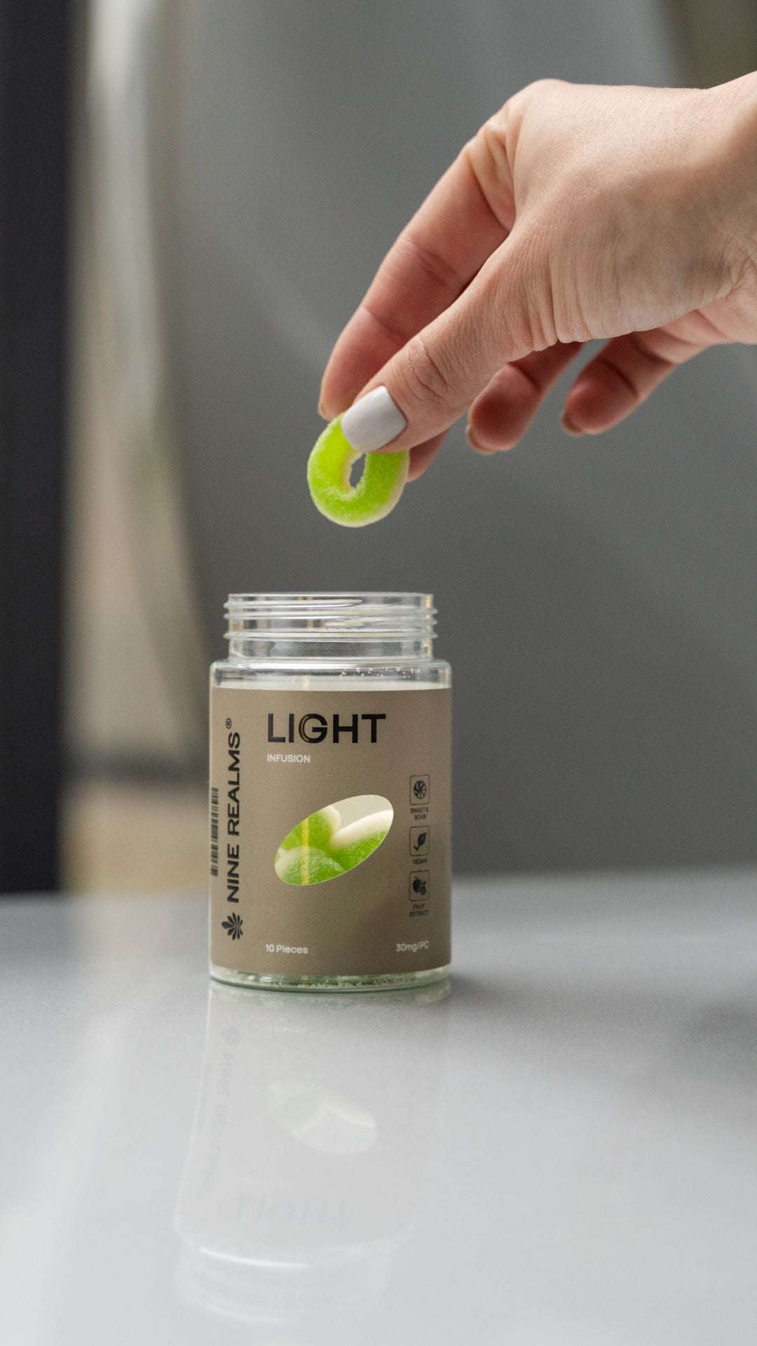 Eine Hand nimmt ein 10-HC-Gummibärchen (Nine Realms LIGHT Infusion) aus einem Glas