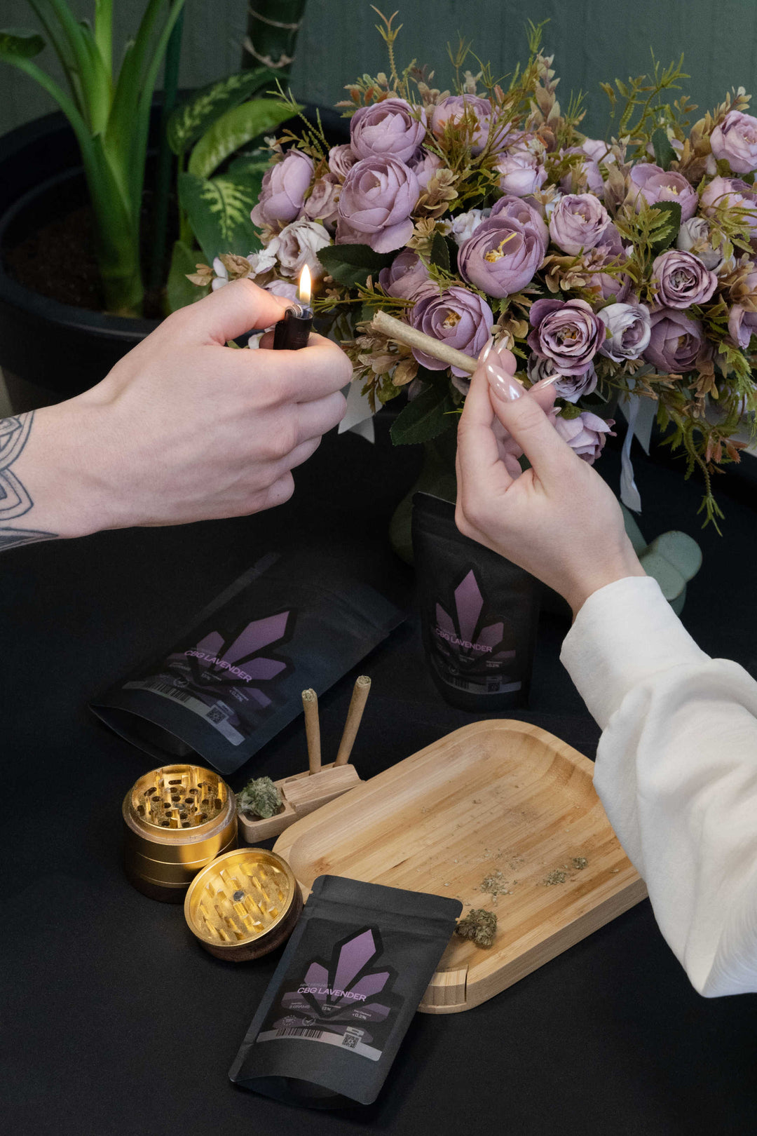 Female holding pre-rolled joint and man holding lighter with cannabis flower and grinder on the tray