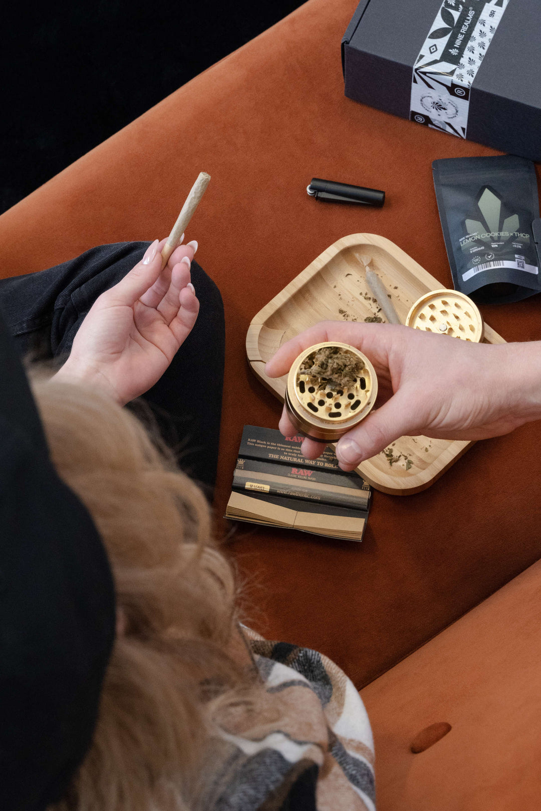 Female holding weed pre-rolled joint with cannabis flower buds in the grinder and tray